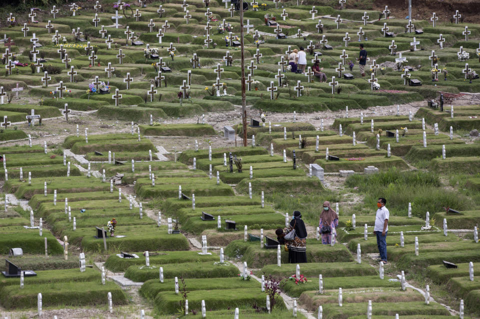 People visit the graves of family members at the special section of a cemetery allocated for the victims of COVID-19 in Medan, North Sumatra, Indonesia, Monday, Jan. 25, 2021. Indonesia has reported more cases of the virus than any other countries in Southeast Asia. (AP Photo/Binsar Bakkara)