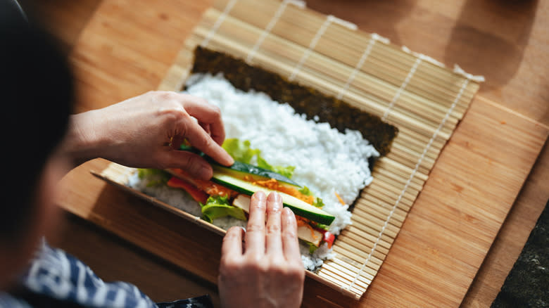 filling nori sheet with vegetables on bamboo mat