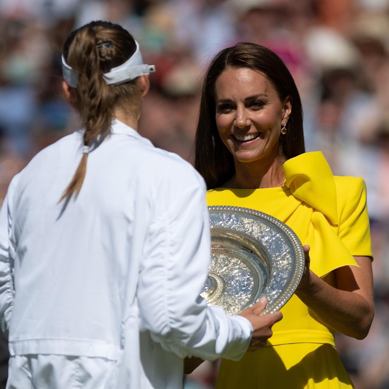  Kate Middleton in a yellow dress presenting a trophy to a tennis player 