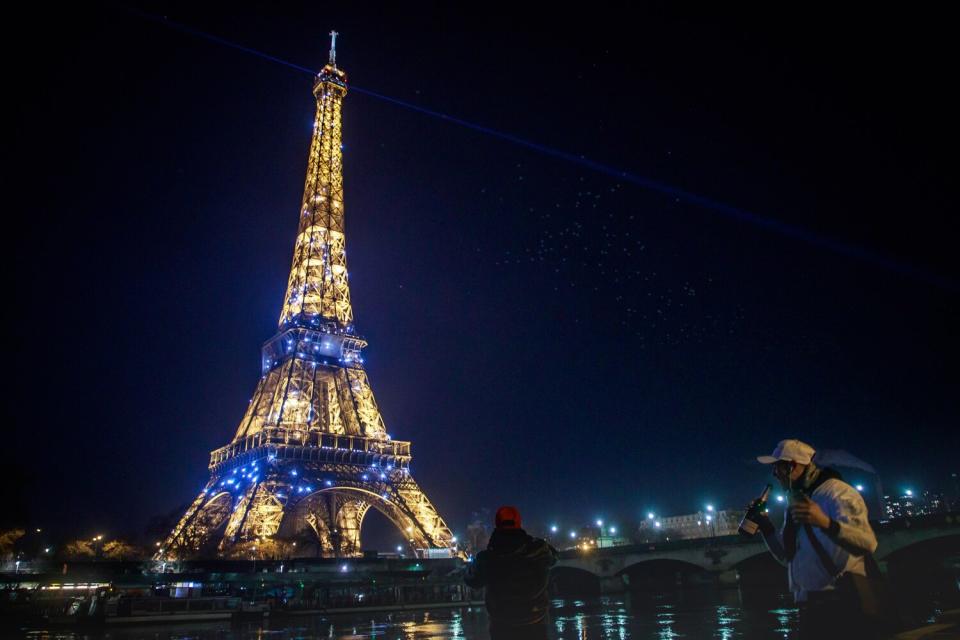 People drink champagne on the banks of the Seine in front of the glittering Eiffel Tower