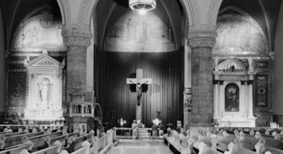A black and white photograph of the interior of an ornate cathedral with a crucifix in the center.