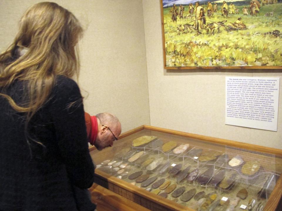 Visitors examine a new Montana Historical Society exhibit in Helena, Mont., on Wednesday, Feb. 12, 2014, showing artifacts discovered at a site at least 12,600 years old. The exhibit opened in conjunction with the release of research that found that people from the 12,600-year-old Clovis culture were direct ancestors of many of today's native peoples in the Americas. (AP Photo/Matt Volz)