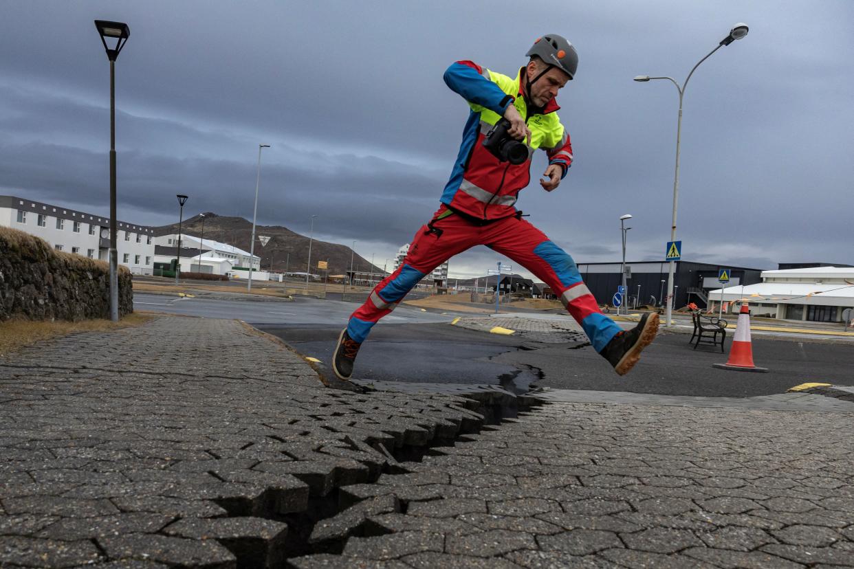 A member of search and rescue team jumps over the crack in a road in the fishing town of Grindavik (REUTERS)