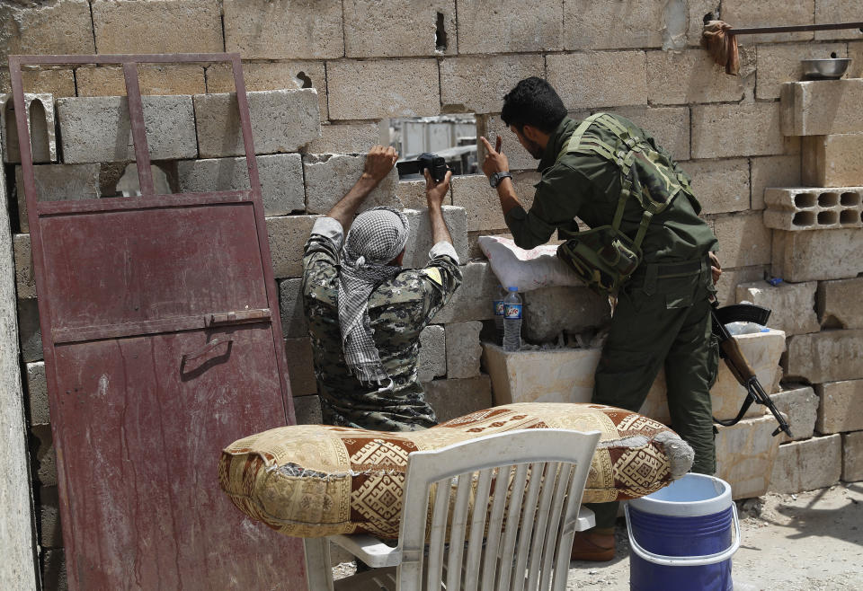 FILE - In this July 17, 2017 file photo, U.S.-backed Syrian Democratic Forces (SDF) fighters use their video camera through a hole as they film a street controlled by Islamic State militants, on the front line on the western side of Raqqa, northeast Syria. A year after it was routed from Iraq following a three-year devastating war that left Iraqi cities in ruin, the Islamic State group is fighting to hang on to its last enclave in Syria, engaging in deadly battles with U.S.-backed forces in the country's east near the Iraqi border. (AP Photo/Hussein Malla, File)