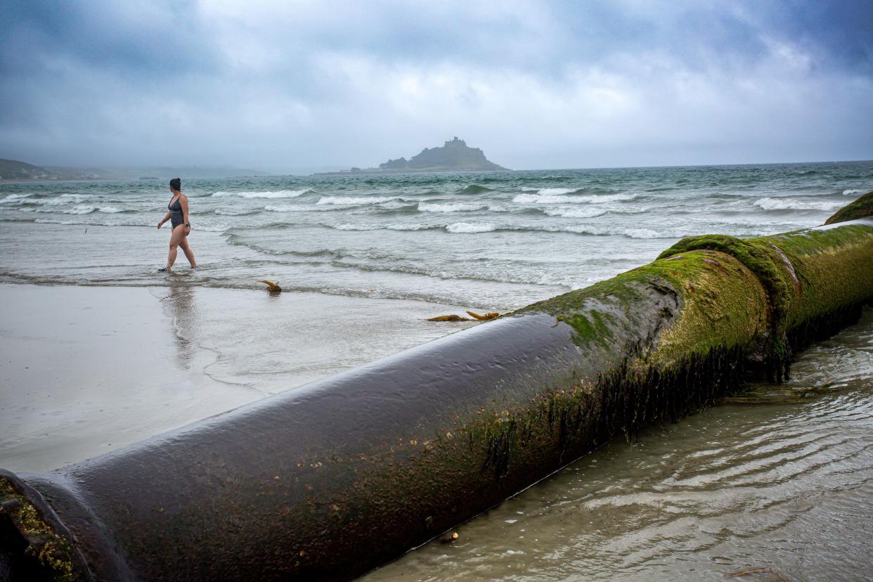 Swimmer walks by outflow pipe at Longrock beach between Penzance and Marazion in Cornwall , United Kingdom.