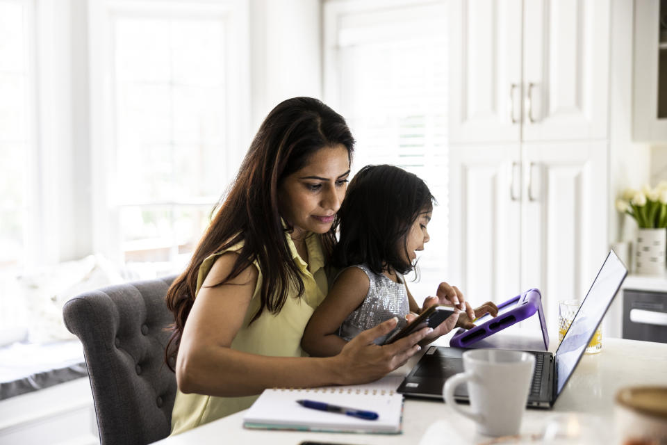 Mother using laptop and smartphone while holding toddler daughter