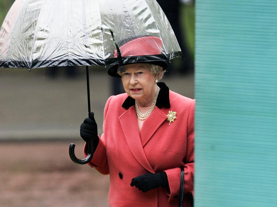 Queen Elizabeth wearing a pink coat and holding an umbrella.