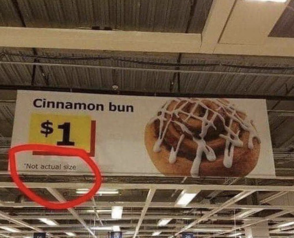 Store sign advertising a cinnamon bun for $1 with the note "Not actual size" humorously circled in red, suggesting the bun is not as large as pictured