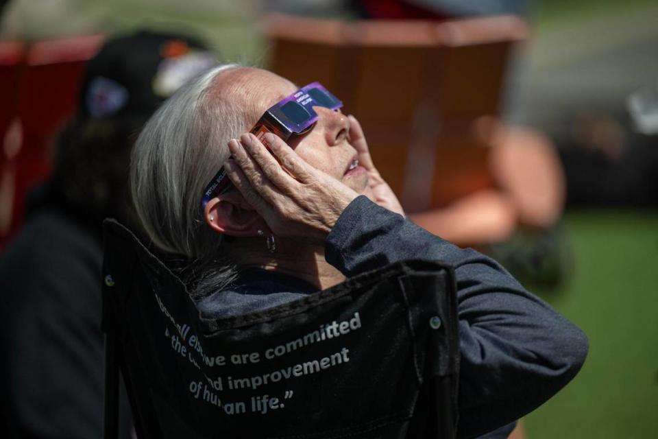 A woman watches the solar eclipse during a watch party at The Lawn at Legends Outlets on Monday, April 8, 2024, in Kansas City, Kansas. A solar eclipse happens when the Moon passes between the Sun and Earth, blocking the face of the Sun.
