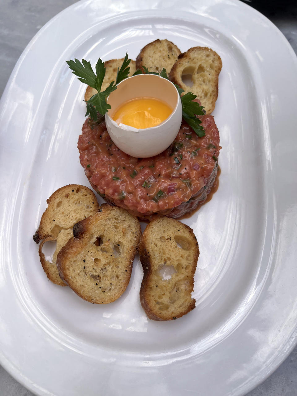 raw egg on top of beef tartare with crostini toasted bread around the outside