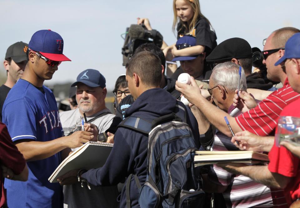 Texas Rangers' Yu Darvish, left, of Japan, signs autographs after a morning workout and throwing session during spring training baseball practice, Tuesday, Feb. 18, 2014, in Surprise, Ariz. (AP Photo/Tony Gutierrez)