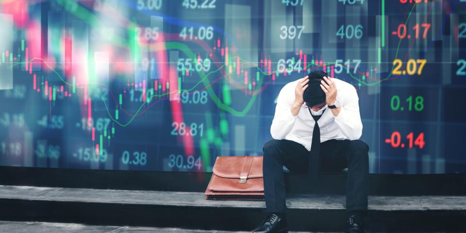 Stressed trader sitting on a walkway with a digital stock market portraying volatility in the background