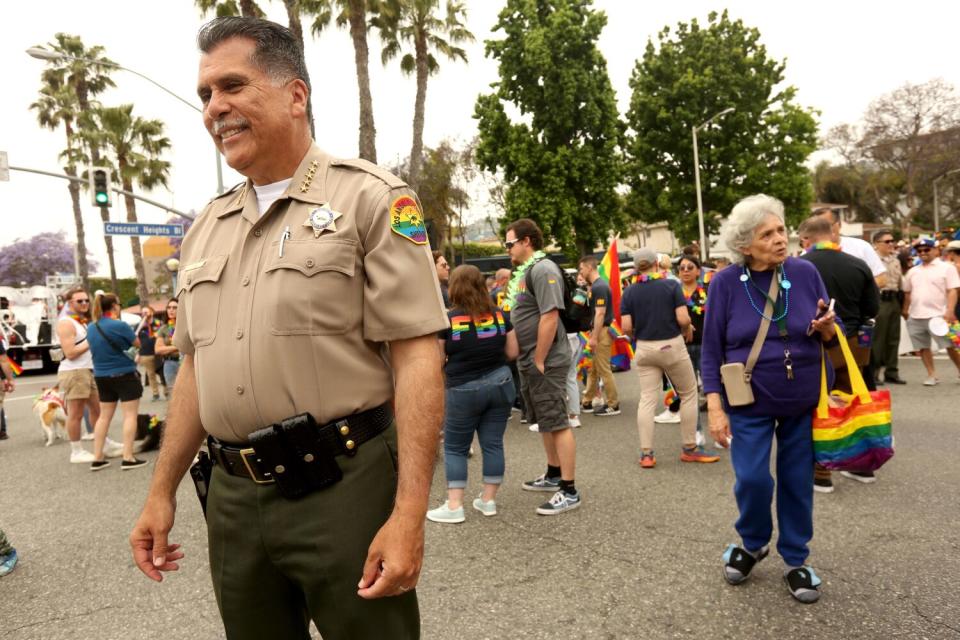 Among a crowd, Los Angeles County Sheriff Robert Luna smiling in uniform with a rainbow-colored patch on his sleeve