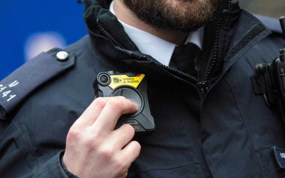 A police officer in uniform demonstrates a body-worn camera