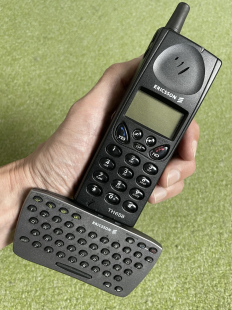 A hand holding an old Ericsson TH688 mobile phone with a flip-out QWERTY keyboard