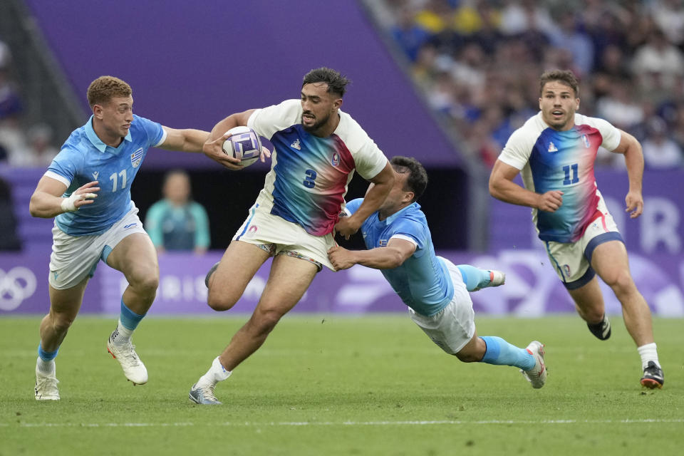 El francés Rayan Rebbadj es derribado por los uruguayos Ignacio Facciolo (izquierda) y Guillermo Lijtenstein, en un partido de rugby 7 de los Juegos Olímpicos, el miércoles 24 de julio de 2024, en Saint-Denis (AP Foto/Tsvangirayi Mukwazhi)