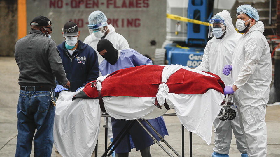 A body wrapped in plastic that was unloaded from a refrigerated truck is handled by medical workers wearing personal protective equipment due to COVID-19 concerns, Tuesday, March 31, 2020, at Brooklyn Hospital Center in Brooklyn borough of New York. (AP Photo/John Minchillo)