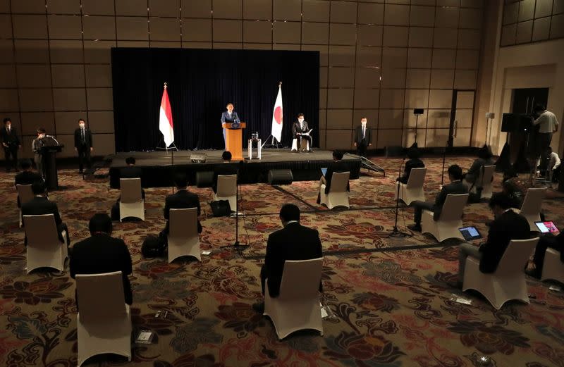 Japanese PM Suga speaks as members of the media sit spaced apart to maintain physical distancing during a press conference in Jakarta
