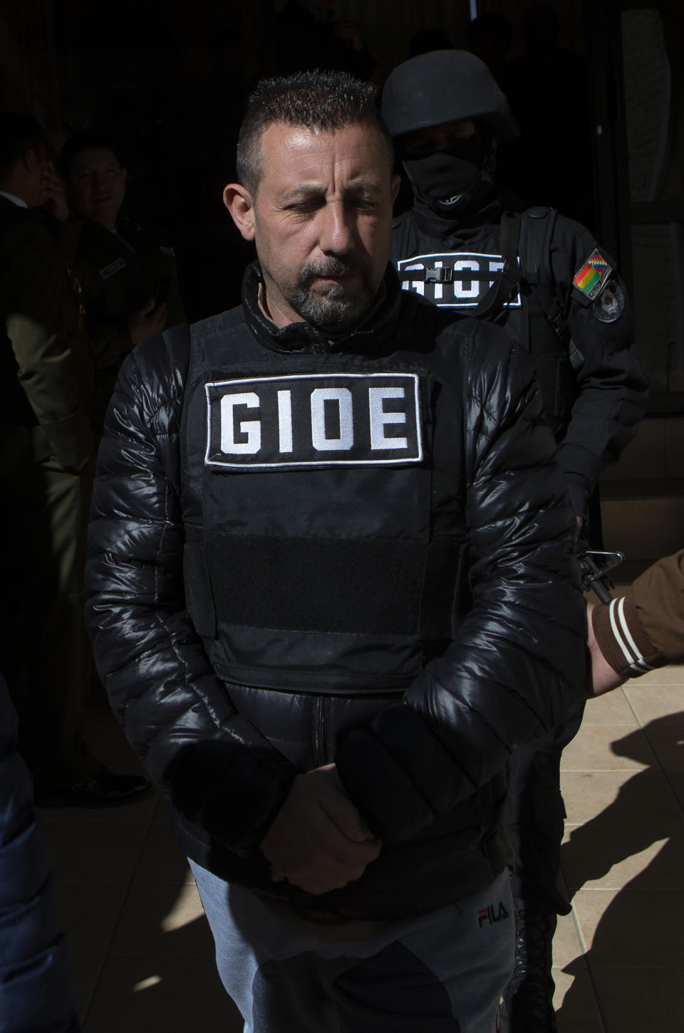 Alleged drug kingpin Paolo Lumia, wearing a bulletproof vest is escorted to a waiting vehicle by anti-drug officers, after a media presentation in La Paz, Bolivia, Thursday, July 4, 2019. Authorities in Bolivia arrested Lumia in the Bolivian city of Cochabamba on Wednesday night. There is an international arrest warrant out for the Italian citizen. (AP Photo/Juan Karita)