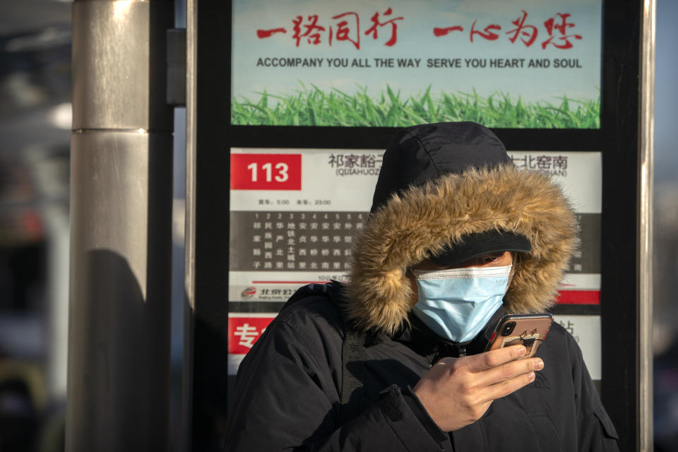 A woman wearing a face mask to protect against the spread of the coronavirus waits at a bus stop during the morning rush hour in Beijing, Wednesday, Dec. 30, 2020. Beijing has urged residents not to leave the city during the Lunar New Year holiday in February, implementing new restrictions and mass testings after several coronavirus infections last week. (AP Photo/Mark Schiefelbein)