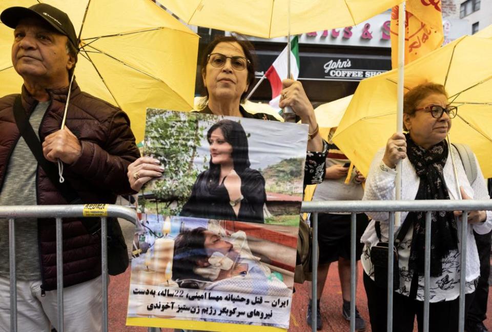 A woman holds a poster that shows two portraits of a young woman. In the bottom photo, the woman is in a hospital bed. 