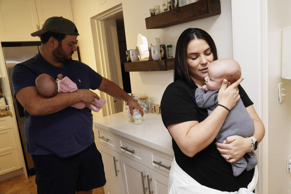 Lissette Fernandez holds their newborn son Luca as her husband George holds their daughter Lexi while also getting their bottles ready, Tuesday, May 24, 2022, in Coral Gables, Fla. The Fernandez have family and friends all over the county looking for formula for their newborn twins. (AP Photo/Marta Lavandier)