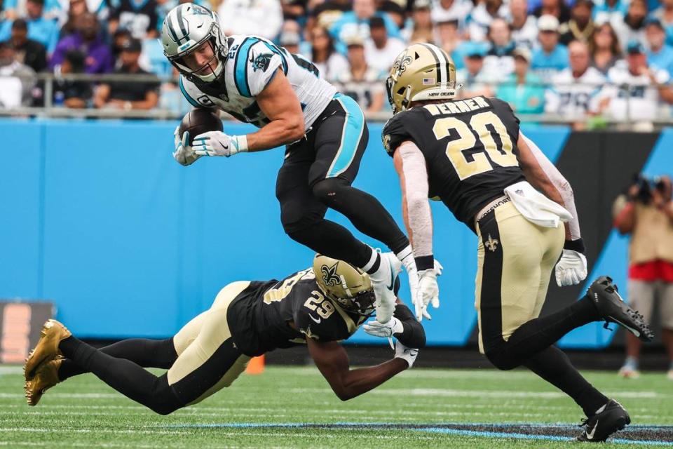 Panthers running back Christian McCaffrey, center, jumps through the grasp of Saints cornerback Paulson Adebo during the game at Bank of America Stadium on Sunday, September 25, 2022 in Charlotte, NC. The Panthers pulled out their first win of the season by defeating the Saints 22-14.