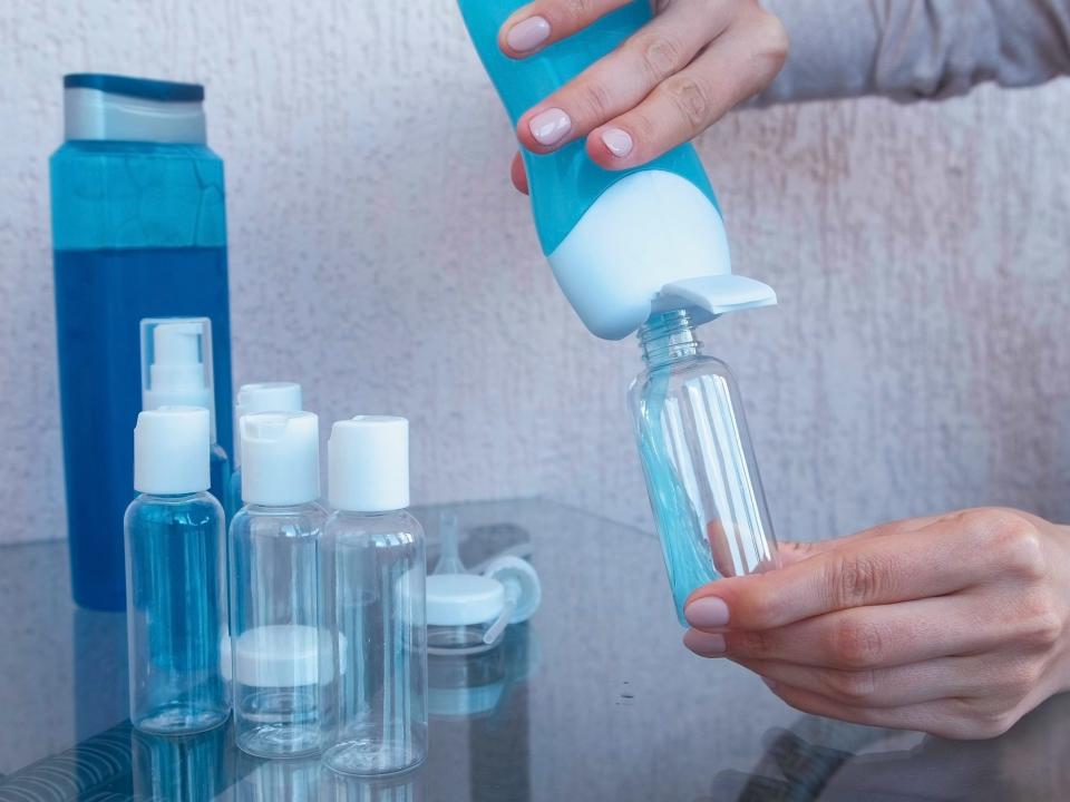 Hand pours blue liquid into small reusable plastic bottle