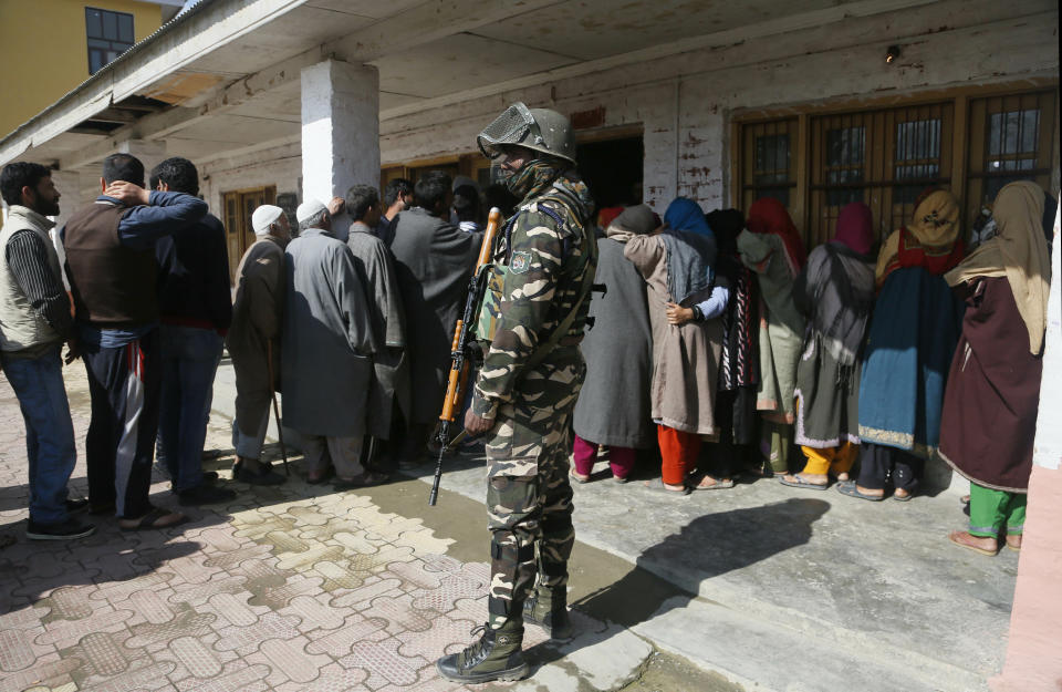 An Indian paramilitary soldier stands guard as Kashmiri voters wait in a queue to cast their votes outside a poling station during the second phase of India's general elections, on the outskirts of Srinagar, Indian controlled Kashmir, Thursday, April 18, 2019. Kashmiri separatist leaders who challenge India's sovereignty over the disputed region have called for a boycott of the vote. Most polling stations in Srinagar and Budgam areas of Kashmir looked deserted in the morning with more armed police, paramilitary soldiers and election staff present than voters. (AP Photo/Mukhtar Khan)