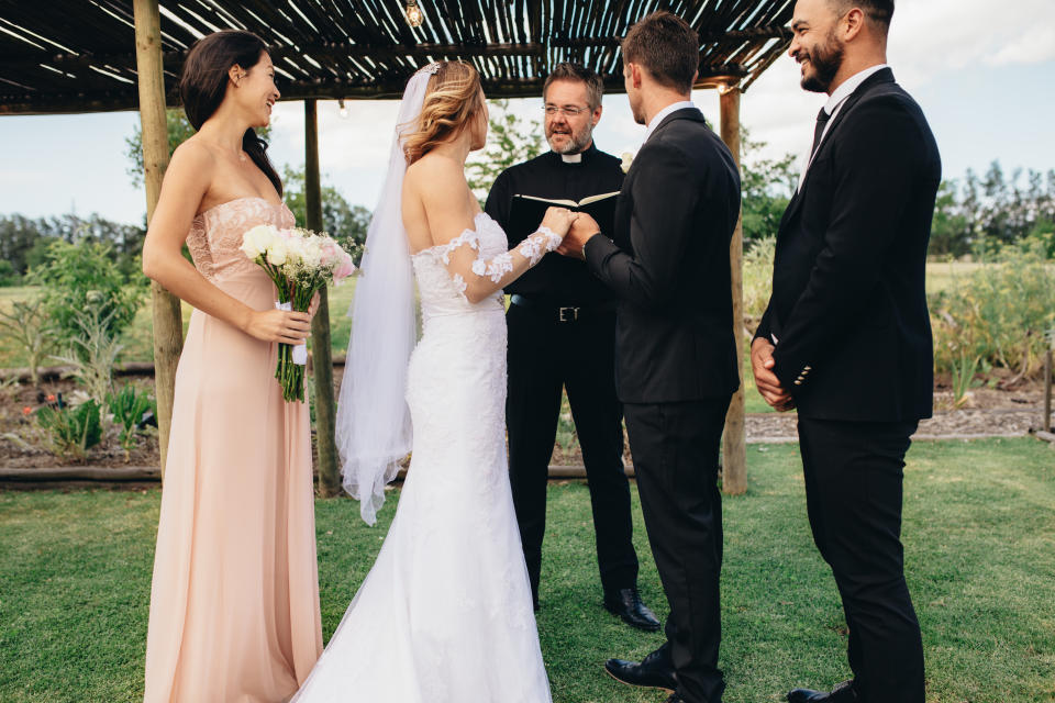 Bride and groom standing in front of priest witness by bridesmaids and best man. Outdoor wedding ceremony of beautiful couple.