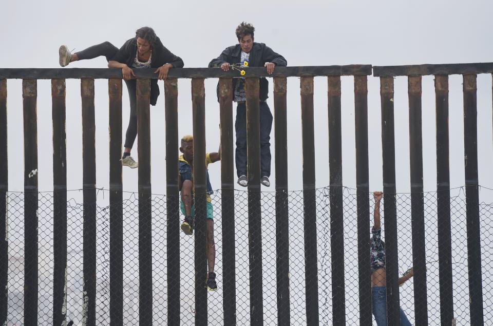 Migrant caravan demonstrators climb the U.S.-Mexico border fence during a rally.