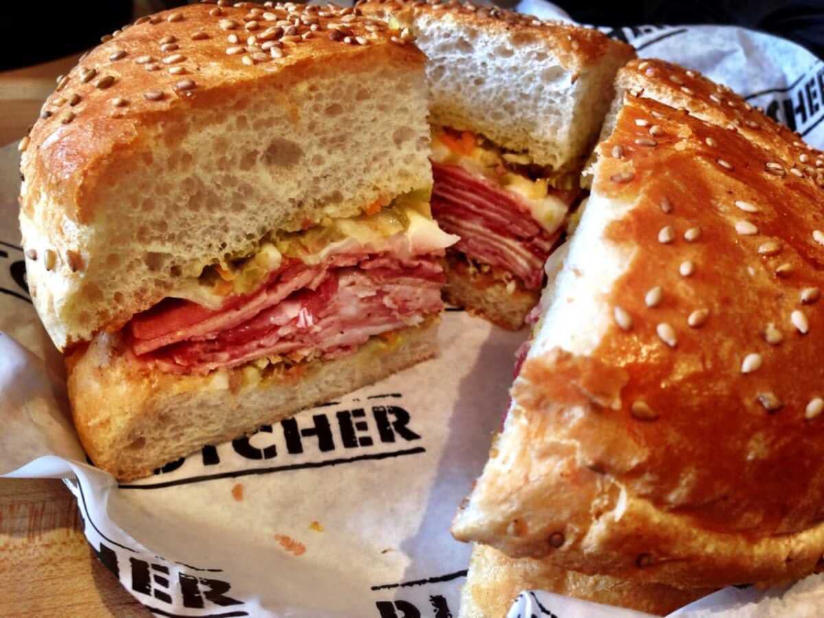 Closeup of Muffuletta on logo white serving paper, Cochon Butcher, New Orleans, on a veneer wooden table