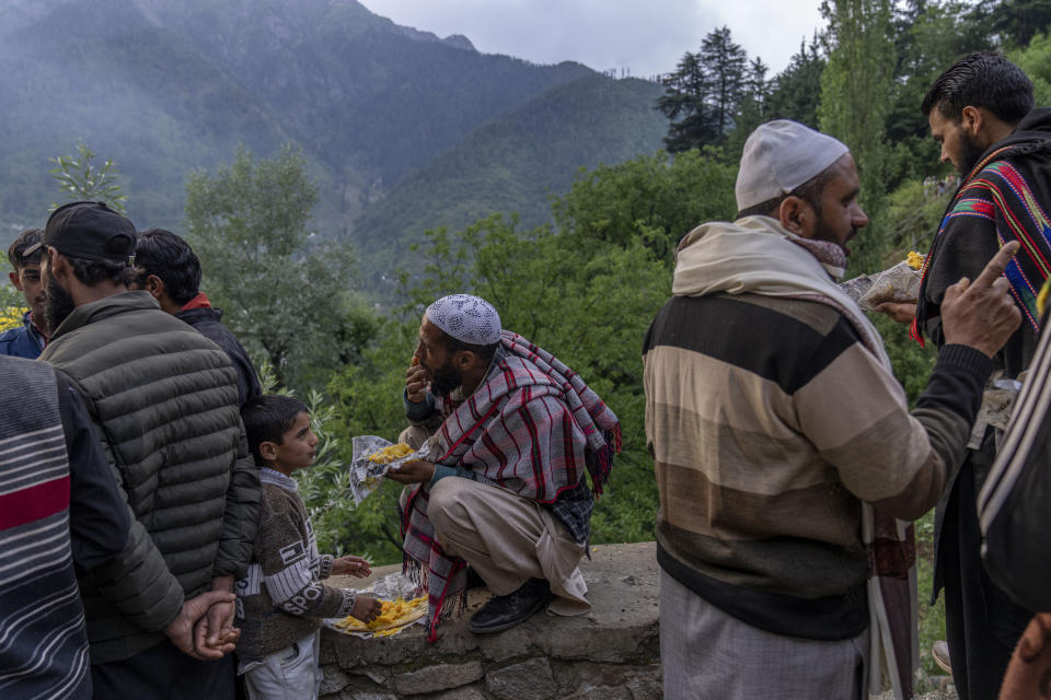 A nomadic Kashmiri man, center, along with his son eats pudding on the road leading to the forest shrine of Sufi saint Mian Nizamuddin Kiyanwi in Baba Nagri, northeast of Srinagar, Indian controlled Kashmir, Saturday, June 8, 2024. (AP Photo/Dar Yasin)