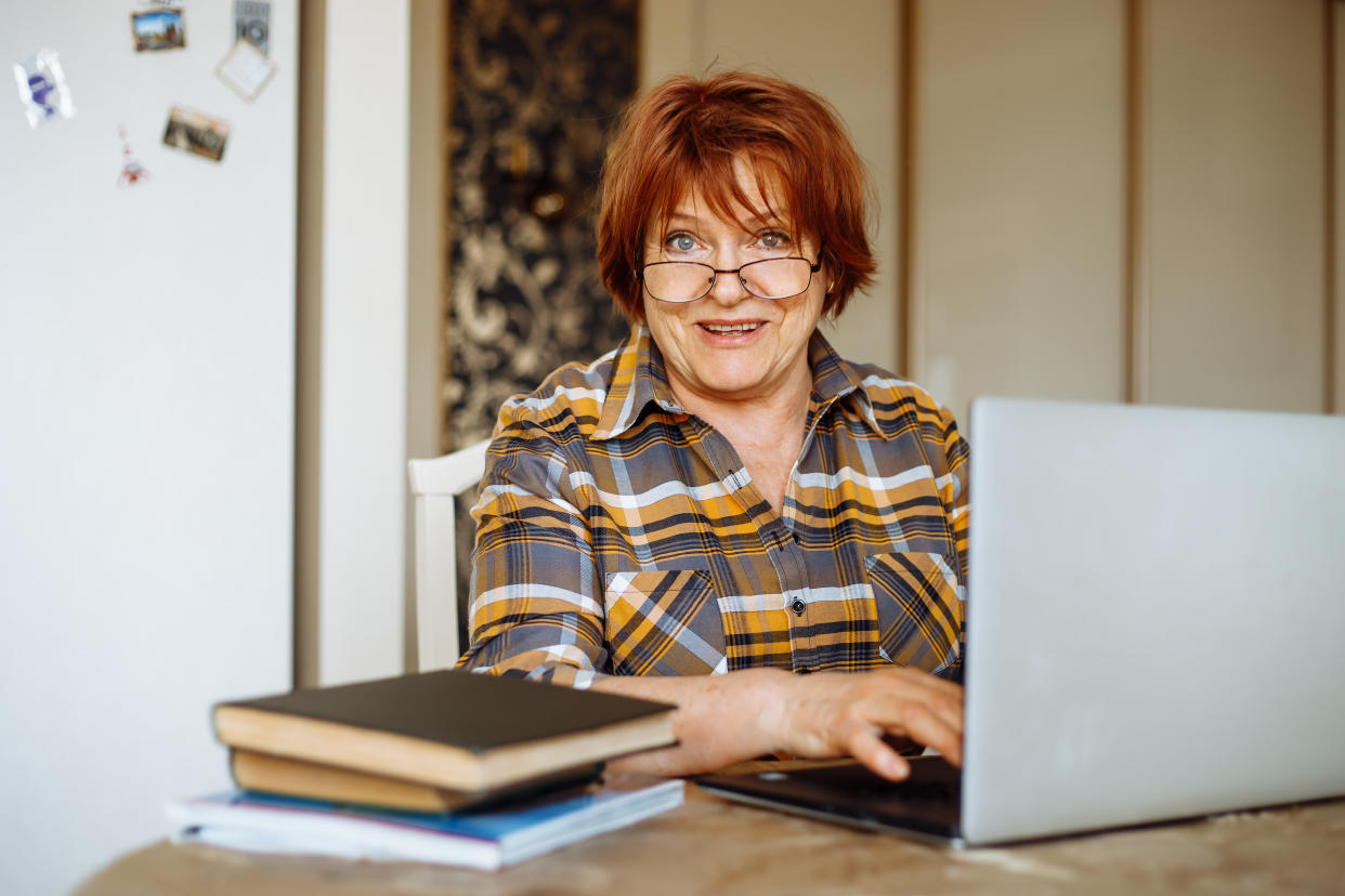 Happy mature lady typing on laptop sitting at desk in room and practicing computer skills. Advanced pensioner using and learning modern technology. Online communication and distant future concept.