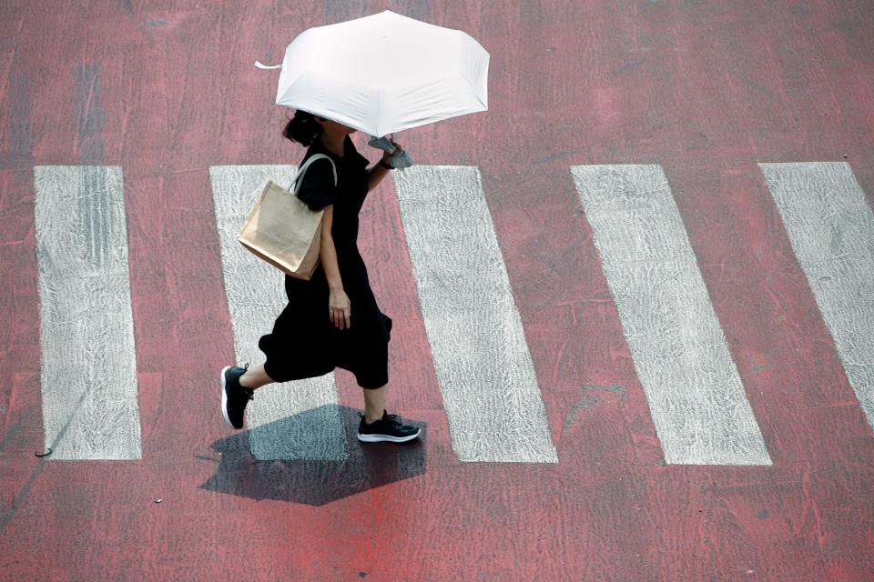 A pedestrian uses an umbrella to protect themselves from sunlight while crossing a street during hot weather in Bangkok, Thailand