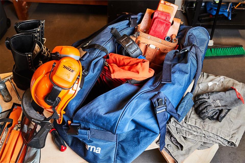 a chainsaw duffle filled with safety glasses, ear muffs, a helmet and face shield, saw chaps, and more safety equipment