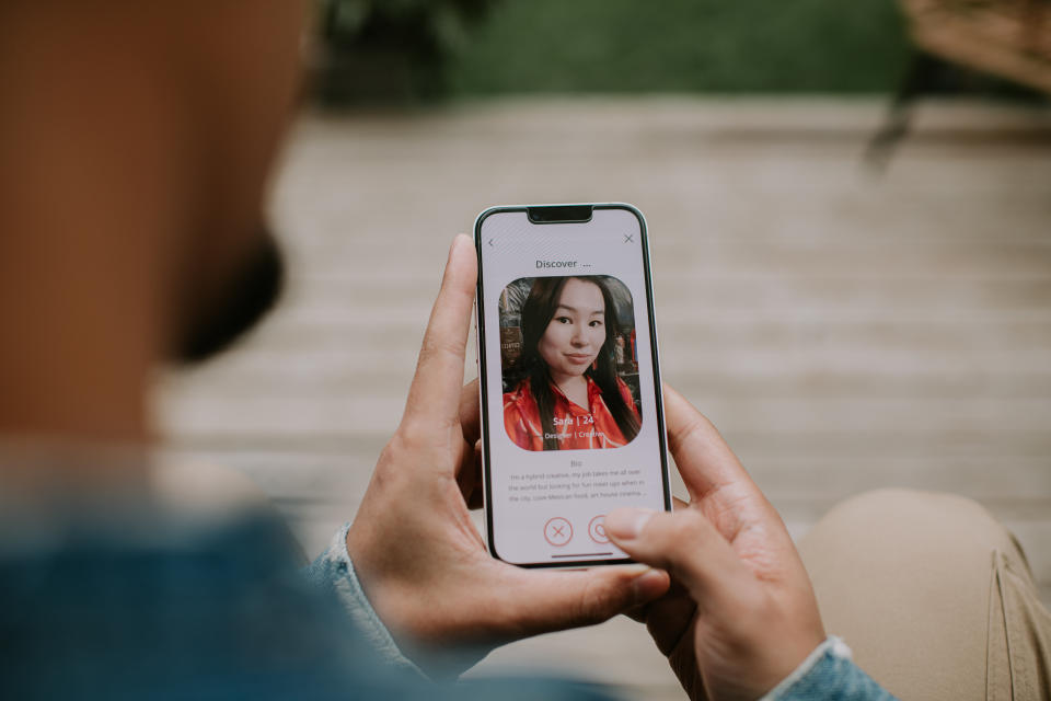 Close-up of a male holding a smart phone, and browsing a dating application, looking at a photo of a woman.