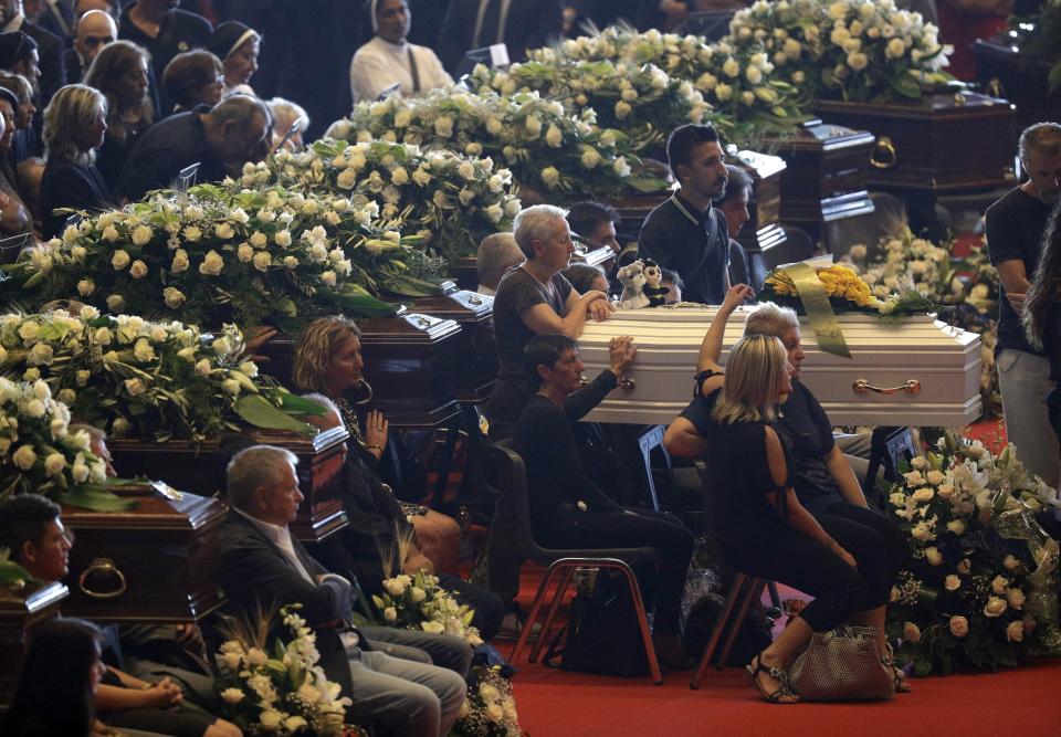 Relatives sit by a small white coffin as they attend a funeral service for some of the victims of a collapsed highway bridge, in Genoa's exhibition center Fiera di Genova, Italy, Saturday, Aug. 18, 2018. Saturday has been declared a national day of mourning in Italy and includes a state funeral at the industrial port city's fair grounds for those who plunged to their deaths as the 45-meter (150-foot) tall Morandi Bridge gave way Tuesday. (AP Photo/Gregorio Borgia)