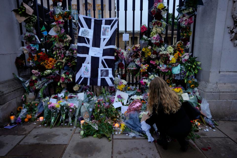 A woman lays flowers and leaves a letter at the gates of Buckingham Palace in London, Friday, Sept. 9, 2022.