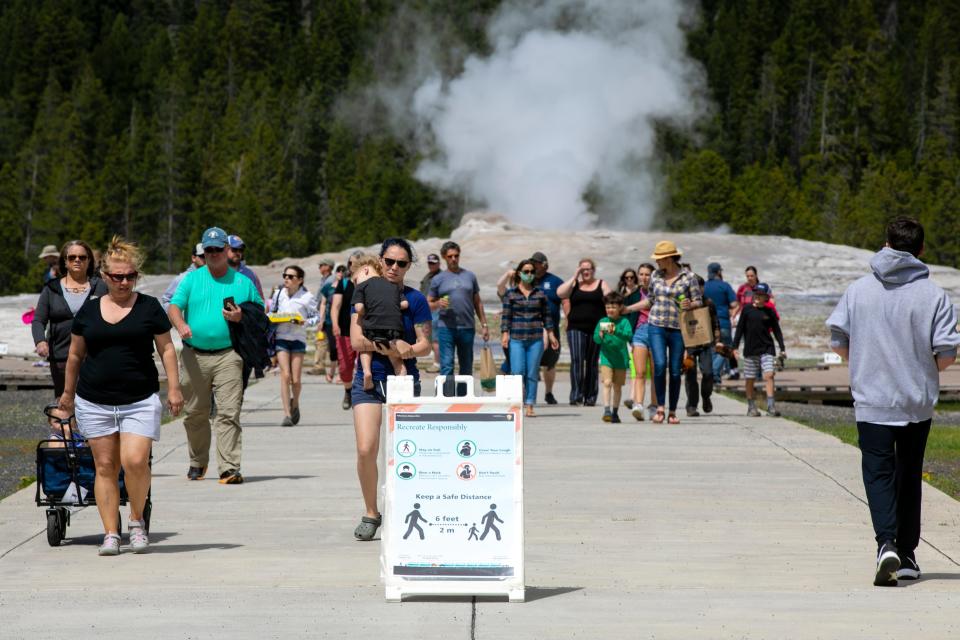 In this Monday, June 1, 2020 photo, visitors walk away from Old Faithful as a sign about COVID-19 safety sits in the sidewalk in Yellowstone National Park in Wyoming.