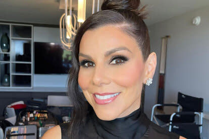 Heather Dubrow smiling with full glam and a top bun in an all black outfit.