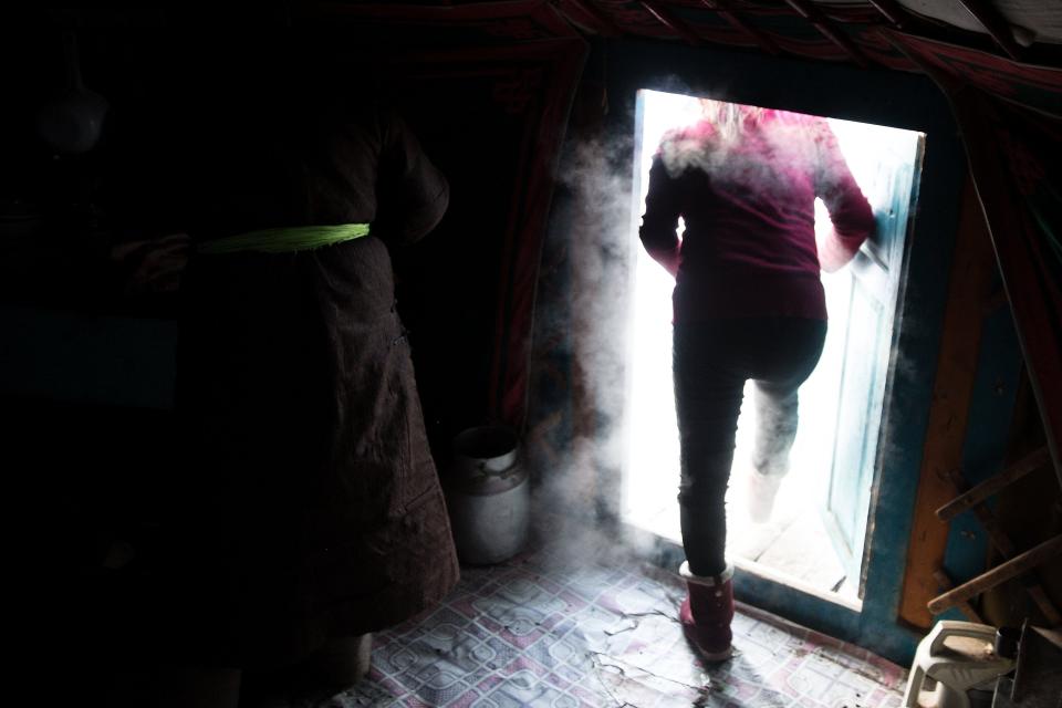 A photo of a women walking out of her shelter and into the bright, snow covered outdoors in a veil of steam.