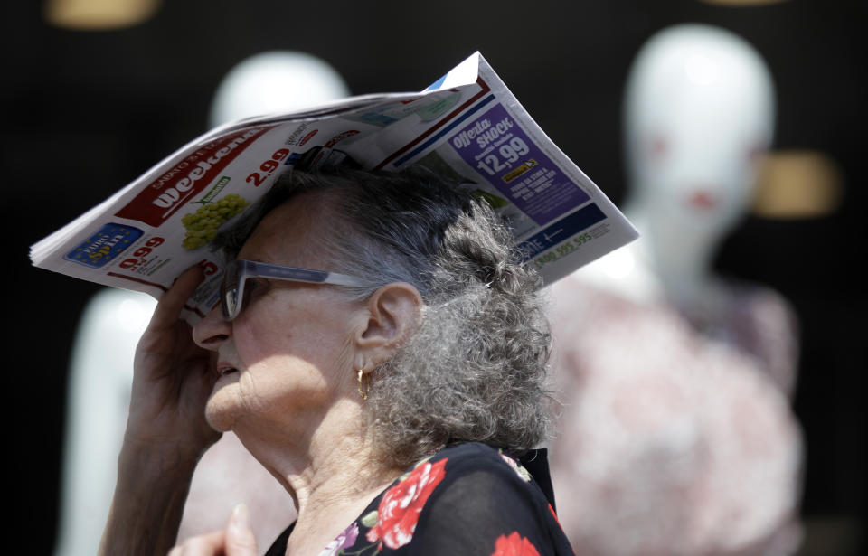 An elderly woman shelters from the hot sun with a newspaper, in Milan, Italy, Thursday, July 25, 2019. Parts of Europe will likely see record-high temperatures on Thursday as much of the continent is trapped in a heat wave, the second in two months. (AP Photo/Luca Bruno)