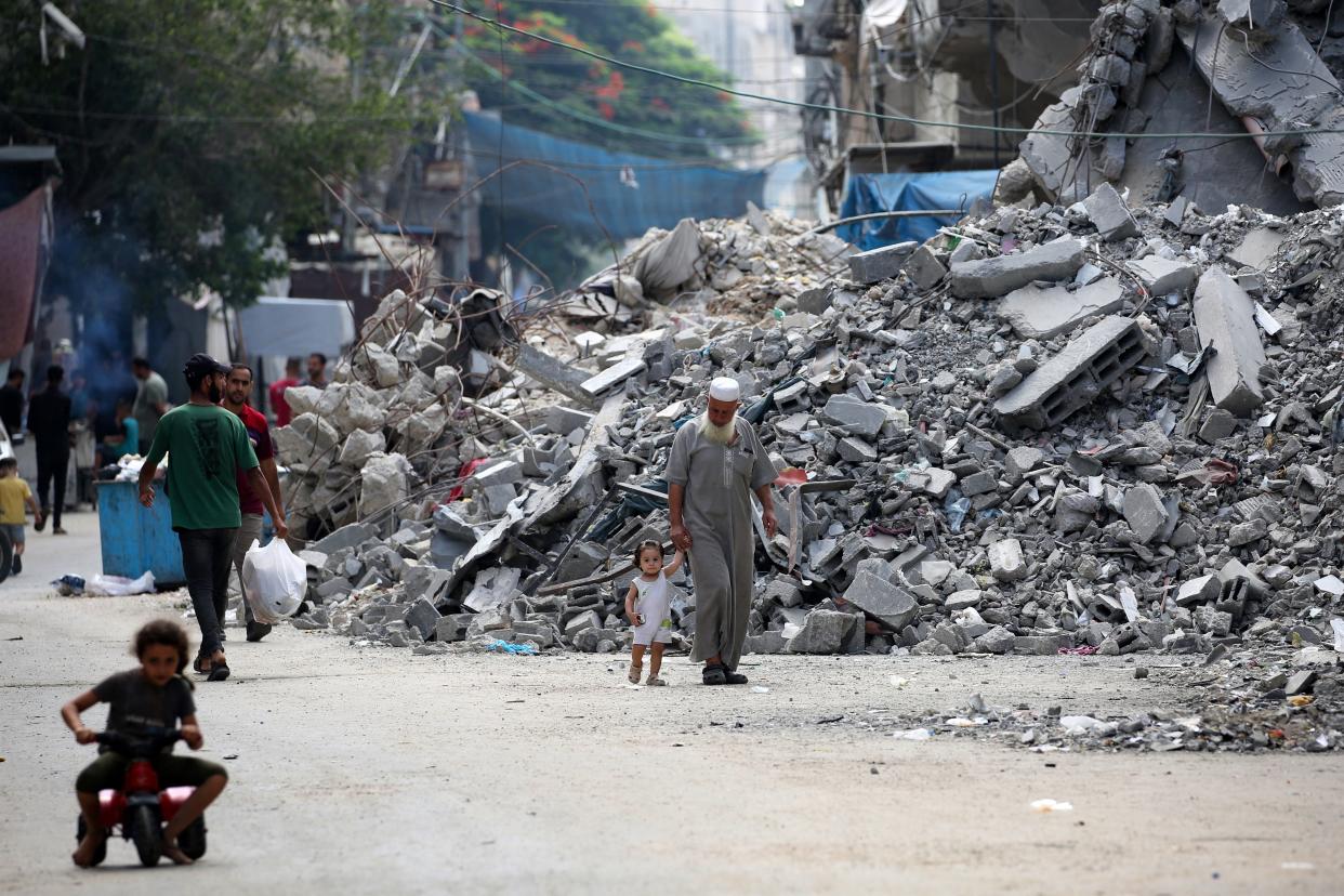 An elderly man holds a child by the hand as he walks past a building levelled by Israeli bombardment in the Bureij refugee camp in central Gaza Strip (AFP via Getty Images)