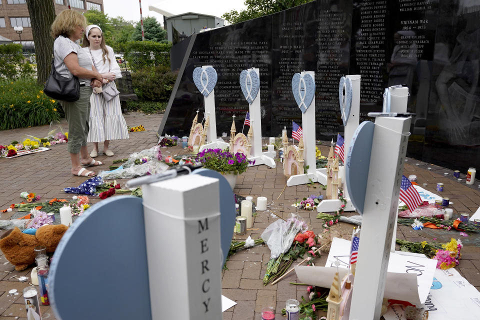 Two women visit a memorial to those killed and wounded in Monday's Fourth of July mass shooting, Wednesday, July 6, 2022, at a veterans memorial in Highland Park, Ill. (AP Photo/Charles Rex Arbogast)