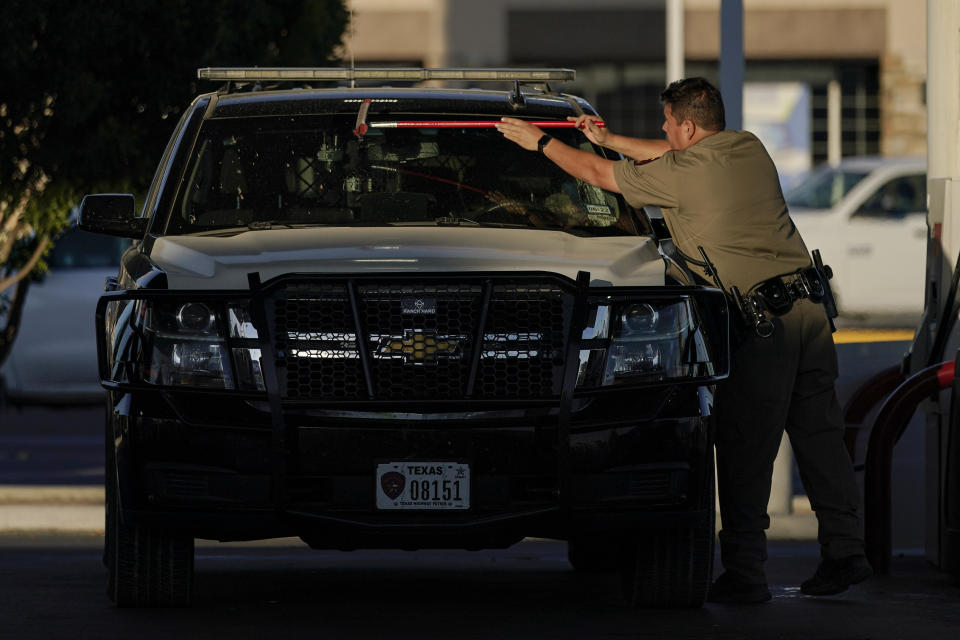 An officer cleans the windshield of a Department of Public Safety vehicle at a gas station, Wednesday, Sept. 22, 2021, in Del Rio, Texas. The “amistad,” or friendship, that Del Rio, Texas, and Ciudad Acuña, Mexico, celebrate with a festival each year has been important in helping them deal with the challenges from a migrant camp that shut down the border bridge between the two communities for more than a week. Federal officials announced the border crossing would reopen to passenger traffic late Saturday afternoon and to cargo traffic on Monday. (AP Photo/Julio Cortez)