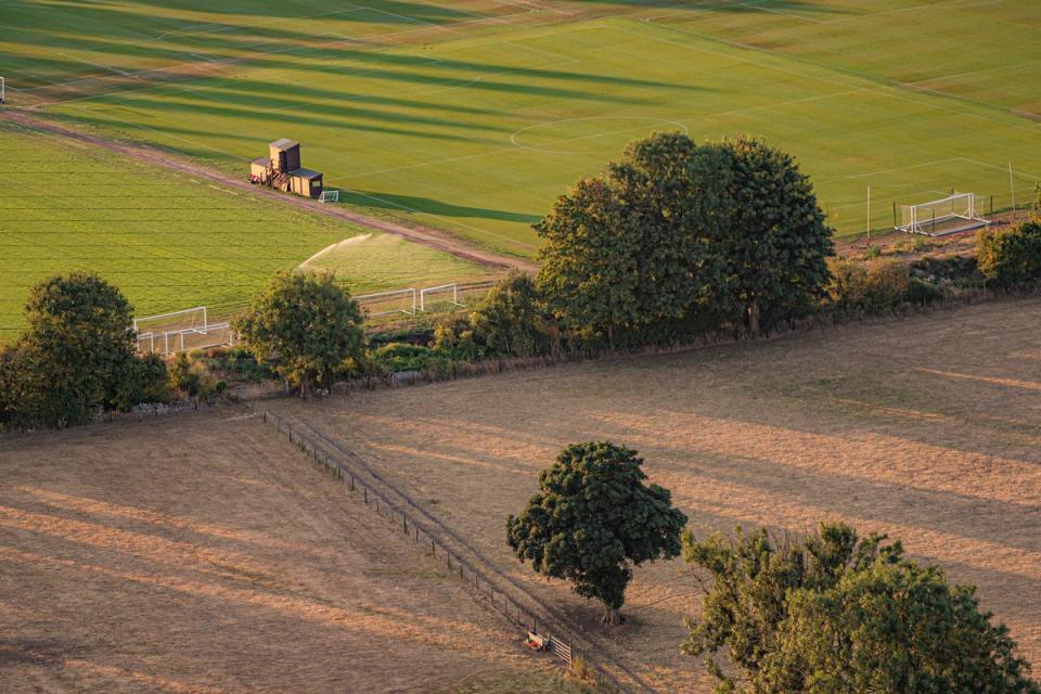 Water is sprinkled onto lush green football pitches adjacent to a parched field (Ben Birchall/PA) (PA Wire)