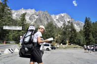 A hiker looks at a map as he walks in a parking lot beneath the Planpincieux glacier, seen at background right, in the Alps on the Grande Jorasses peak of the Mont Blanc massif, in Val Ferret on the south side of the Mont Blanc, near Courmayeur, northern Italy, Friday, Aug. 7, 2020. Some 70 people were evacuated Thursday in the valley below the glacier and roads closed after the threat of collapse the the fast-moving melting glacier is posing to the picturesque valley near the Alpine town of Courmayeur. (Claudio Furlan/LaPresse via AP)