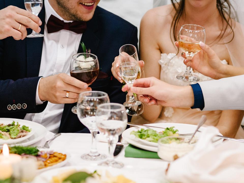 people cheersing wine glasses in front of a groom and bride at a wedding reception
