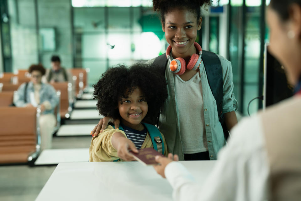 A smiling woman and a child hand over a passport at the airport check-in counter.